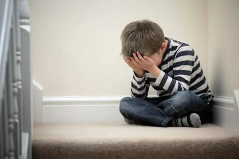 sad child sitting in corner crying with head in hands