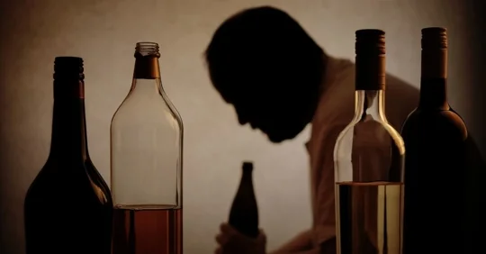Silhouette of a man leaning over a beer bottle, alcohol bottles in the front. Alcohol addiction.