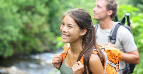 Photo of a close-up of two hikers in focus, with a river and trees in the background.