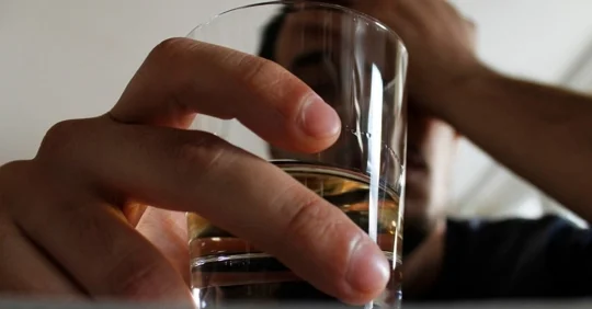 Close up of a person holding a glass with brown liquid.