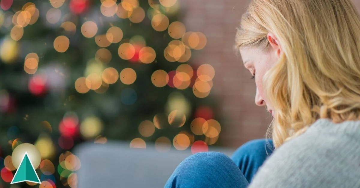 Female with her head down looking somber in front of a Christmas tree