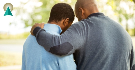 Dad with his arm wrapped around his young adult aged son.