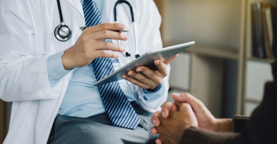 Photo of an unidentifiable doctor holding an iPad talking to a patient.