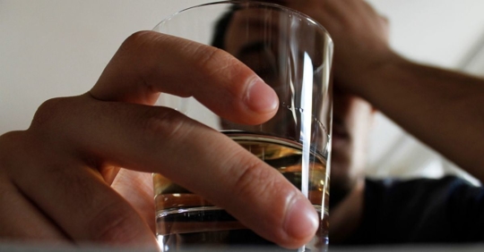 Close up of a person holding a glass with brown liquid.