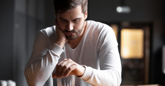 Man with his hand on a drink at a bar, relapsing during alcohol addiction recovery.