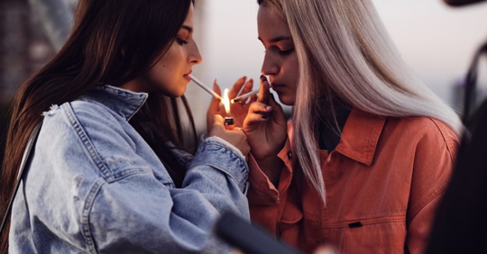 Two young adults lighting cigarettes.