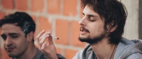 man against brick wall looking at marijuana cigarette