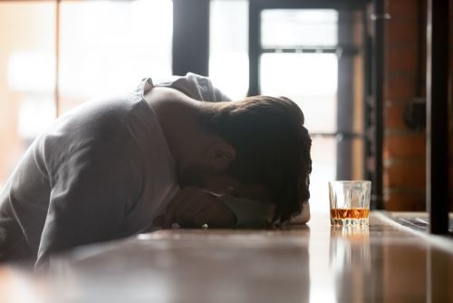 depressed man at a bar with his head in his arms