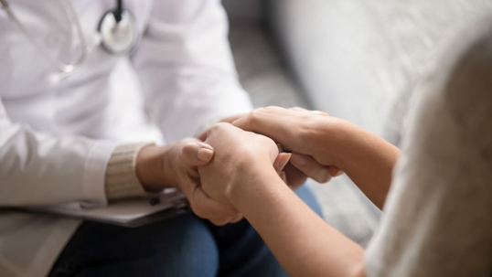 Close up horizontal image doctor in white uniform holding hands of female patient