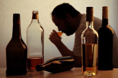 man drinking behind several empty bottles of alcohol