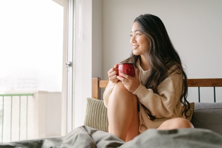 woman-sitting-on-bed-with-coffee-looking-out-window