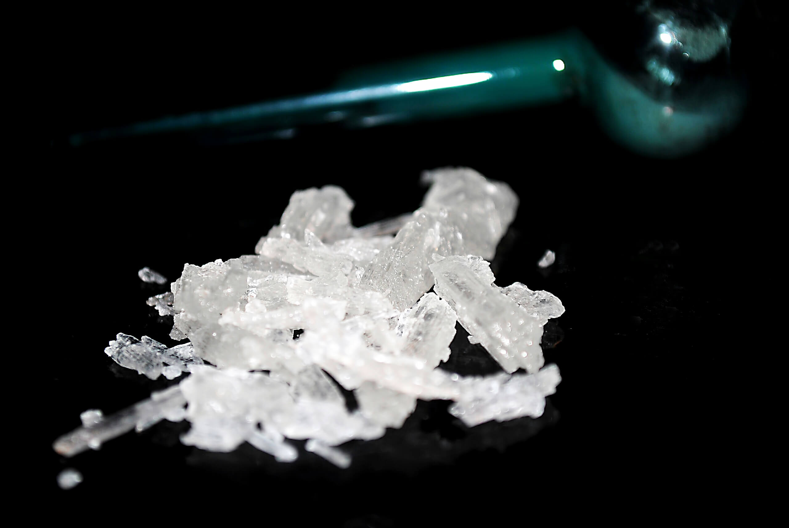 small pile of methamphetamine crystals with a meth pipe in background